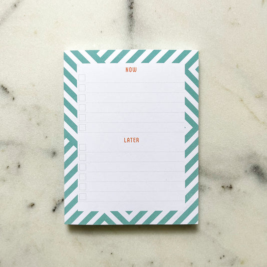 Notepad with lines and check boxes over a geometric teal / aqua pattern on a marble table top