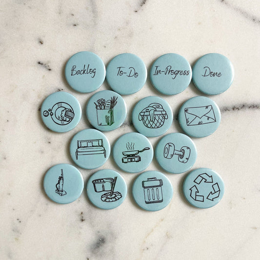 Set of 15 blue magnets on a marble table top. There are four title magnets which read "Backlog", "To-Do", "In-Progress", and "Done".The other eleven magnets represent a different chore. The chores represented are "Take out the recycling", "Go grocery shopping", "Make the bed", "Take out the trash", "Cook a meal", "Do the dishes", "Workout", "Vaccuum", "Mop", "GEt the mail", and "Do the laundry"